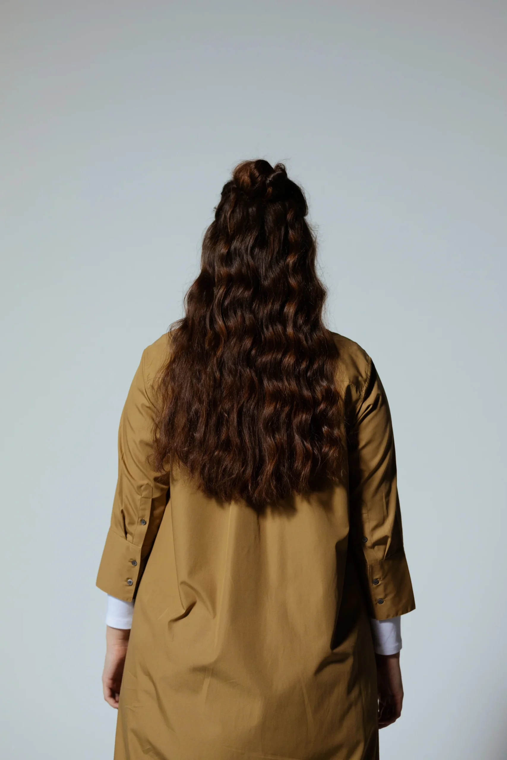 A person with long brown hair worn partly up and a tan coat, seen from behind