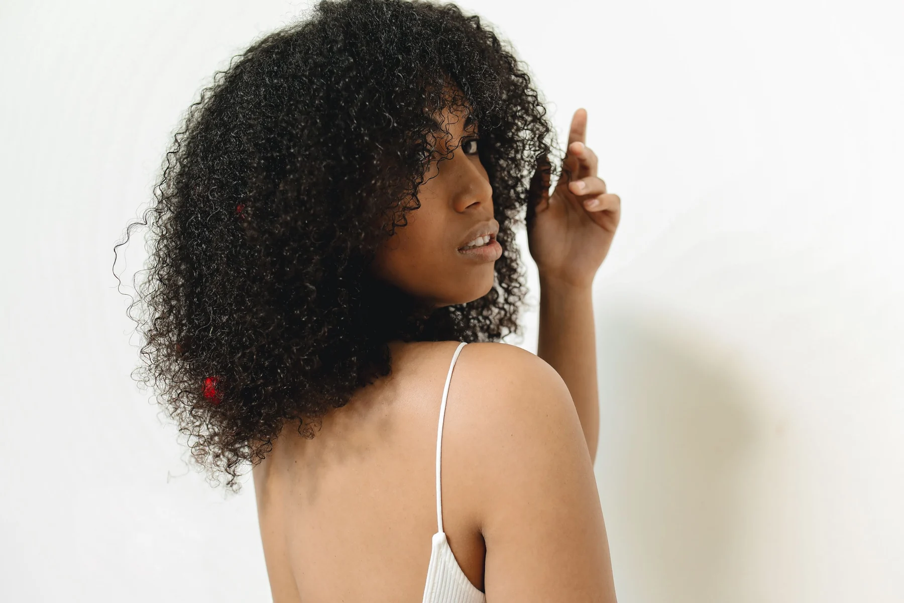 A woman with dark curls looking over one shoulder against a pale background