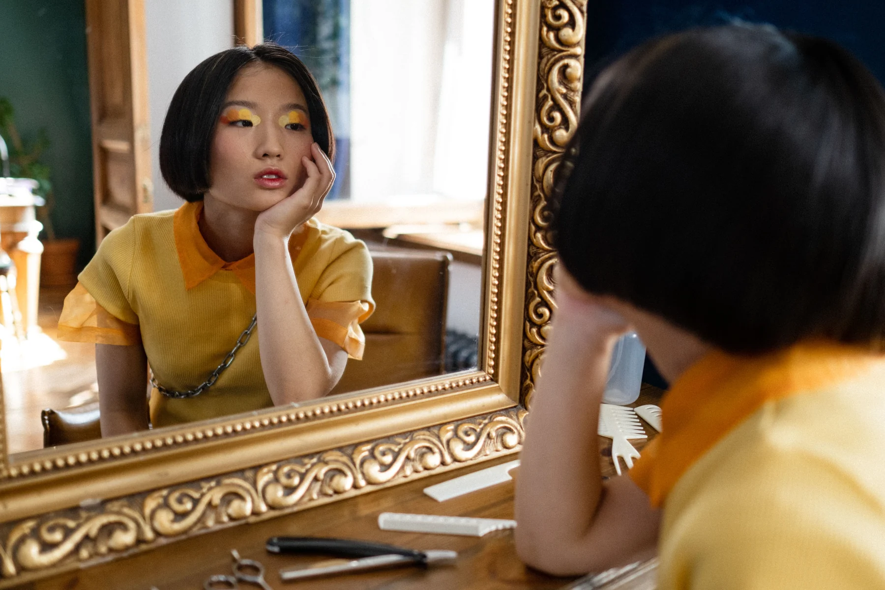 A person with a short bob looking into an ornate mirror beside styling tools